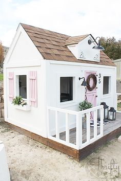 a small white house with pink shutters on the front and side windows, sitting next to a fence