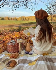 a woman sitting on a blanket in the leaves reading a book and looking at her food