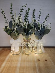 three glass vases with flowers and lights in them