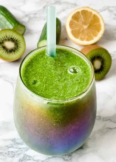 a green smoothie in a glass with a straw next to sliced kiwis