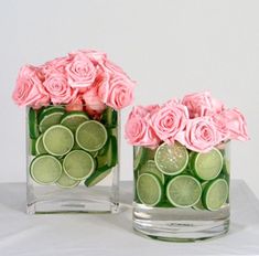 two vases filled with flowers and cucumbers on top of a white table