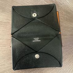 a black leather case sitting on top of a wooden table next to an orange pen