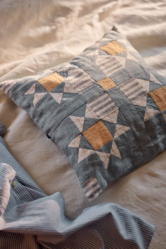 a blue and yellow pillow sitting on top of a bed next to a white blanket