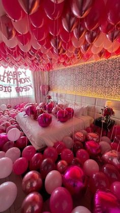 a room filled with lots of pink and white balloons hanging from the ceiling over a bed