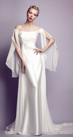 a woman in a white dress posing with her hands on her hips and wearing an off the shoulder cape