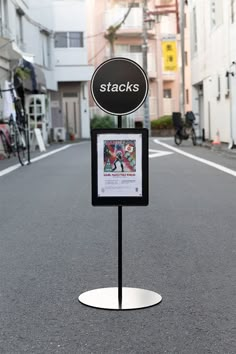 a sign that is sitting in the middle of an empty street with people on bikes behind it