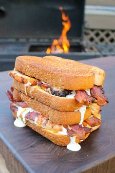 three sandwiches sitting on top of a wooden cutting board next to an open fire pit