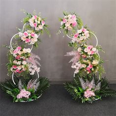 two white metal stands with pink and white flowers on them, surrounded by greenery