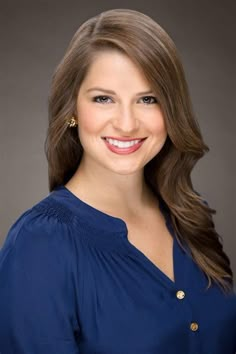 a woman with long brown hair wearing a blue shirt and gold earrings smiling at the camera