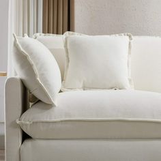 a white couch with two pillows on it's back and one pillow sitting on the arm