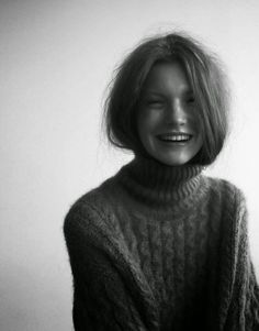 a black and white photo of a smiling woman in a turtle neck sweater with her hair blowing back