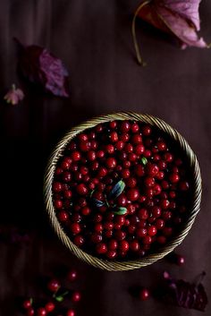 a basket filled with lots of red berries on top of a table next to leaves