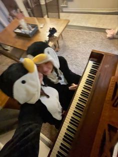 a person in a cow costume sitting at a piano with a stuffed animal on it's head