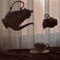 two teapots are pouring water into a cup