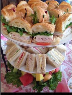 three tiered platter with sandwiches and fruit on the bottom one is filled with watermelon, lettuce, and ham