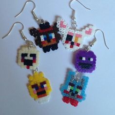 four different colored pixel style earrings hanging from silver earwires on a white surface