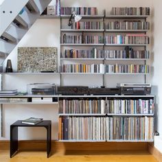 a bookshelf filled with lots of books next to a stair case full of cds