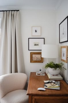 a desk with a lamp, chair and pictures on the wall above it in front of a window