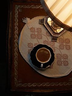 a cup of coffee sitting on top of a saucer next to a table lamp