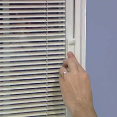 a person is opening the window with their finger and pressing down on the blind in front of them