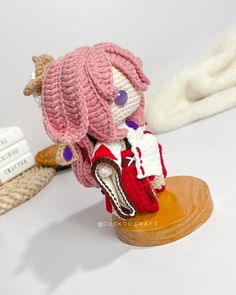 a knitted doll sitting on top of a wooden stand next to a white blanket