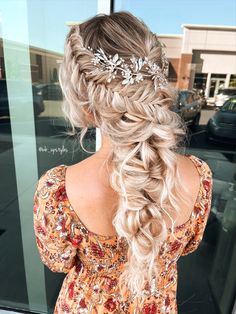 a woman with long blonde hair wearing a braid and flower headpiece in front of a store window