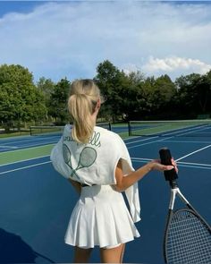 a woman holding a tennis racquet on top of a tennis court with trees in the background