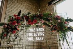 flowers and greenery are arranged in front of a sign that says i was made for loving you, baby