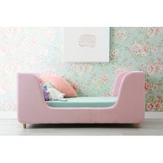 a pink couch sitting in front of a wall with flowers on it and a pillow