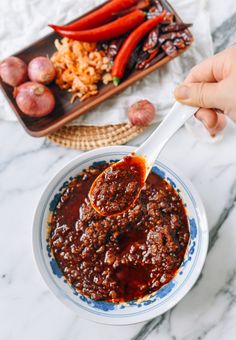 someone is spooning chili sauce into a bowl with onions and garlic on the side