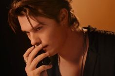 a young man is talking on his cell phone while wearing a black shirt and necklace