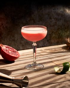 a pink drink sitting on top of a wooden table next to a sliced pomegranate