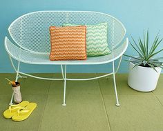 a white bench with two pillows on it next to a potted plant and yellow flip flops