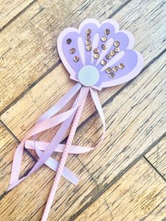 a paper flower with beads on it sitting on a wooden floor next to a pink ribbon