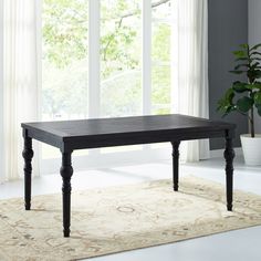 a black table sitting on top of a rug in front of a large window with white curtains