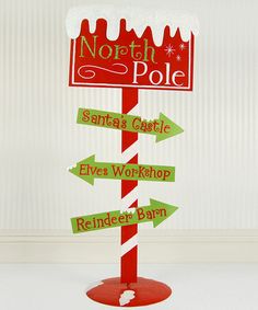 a red and white sign with green arrows pointing to north pole, santa's castle, elves workshop, reindeer barn