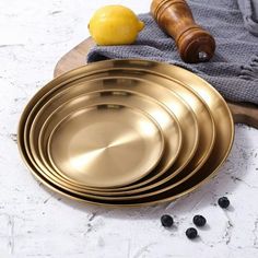 a stack of brass plates sitting on top of a wooden cutting board next to lemons