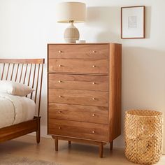 a wooden dresser sitting next to a bed with a lamp on it's headboard