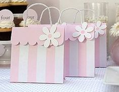 pink and white bags with flowers on them sitting on a table next to cupcakes