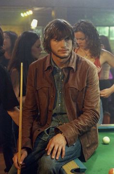 a young man sitting on top of a pool table next to a pool ball rack