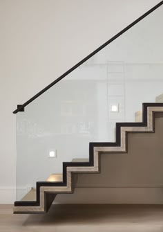 a stair case with glass handrails and black rails on the bottom, in front of a white wall