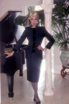 a woman standing next to a piano in a room with columns and potted plants