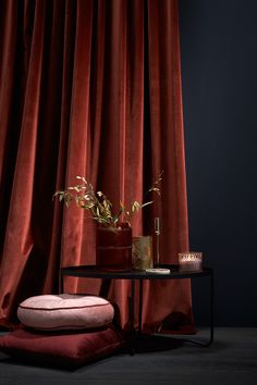 a small table with a plant on it next to a red drapeed curtain