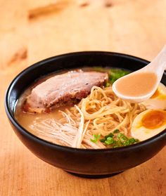 a bowl of ramen with meat, noodles and an egg on the side sitting on a wooden table