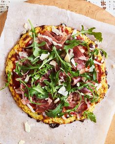 a pizza topped with greens and meat on top of parchment paper