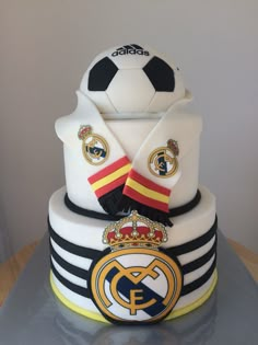 a three tiered cake decorated with soccer balls and crests on the top layer