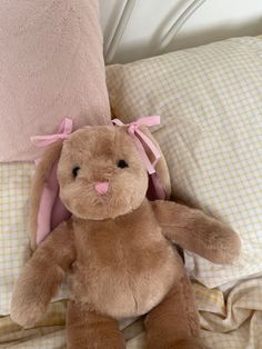 a brown stuffed rabbit sitting on top of a bed next to pillows and blankets with pink bows