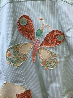 an embroidered butterfly sits on the back of a blue jean jacket with white pinstripe