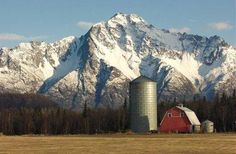 a red barn and silo in front of a mountain range with snow on the top