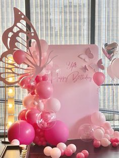 a birthday card with balloons and butterflies on the table in front of a large window